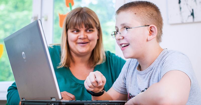 Eine Auszubildende im Bereich Erzieher - praxisintegriert betreut ein Kind, welches grade an einem Laptop arbeitet.