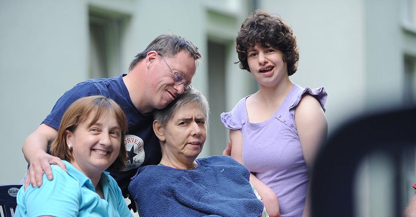 Vier Menschen verschiedenen Alters mit verschiedenen Behinderungen lächeln in die Kamera.
