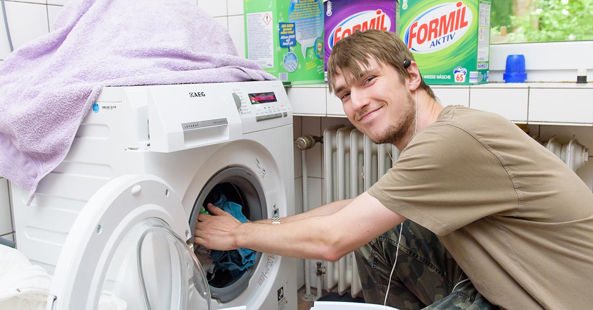 Ein junger Mann packt Wäsche in eine Waschmaschine.